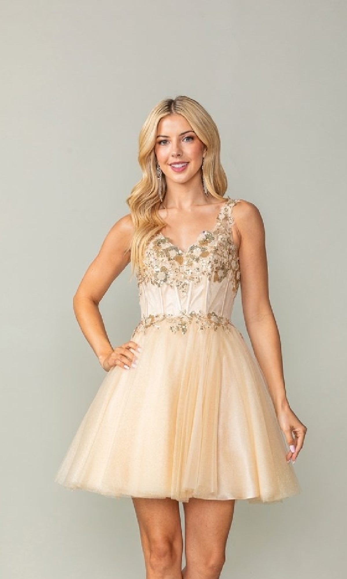 Woman wearing a champagne dress with floral embellishments on a plain background